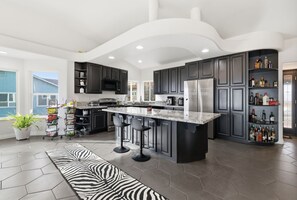 A modern kitchen with dark cabinetry, a central island with bar stools, a built-in microwave, and a wine rack.
