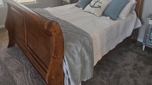 A bedroom with a wooden bed, white bedding, and a nightstand with a lamp.