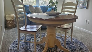 A dining area with a round table, four chairs, a blue patterned rug, and a window with blinds.