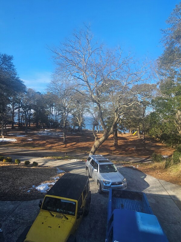 A parking area with several vehicles, including a yellow SUV and a silver car, parked near a tree-lined path.