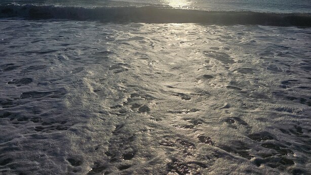 A beach with the sun low on the horizon, casting a reflection on the water.