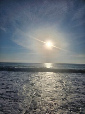 A beach with the sun low on the horizon, casting a reflection on the water.