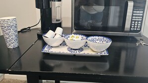 A black table with a microwave, a coffee maker, and three bowls with blue patterns.