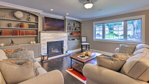 A living room with a fireplace, bookshelves, a sofa set, and a large window.