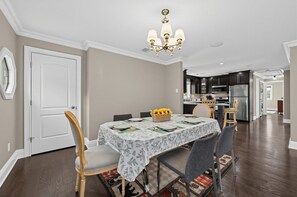A dining area with a table set for four, a chandelier, and a kitchen in the background. - Cozy Glen Cove Apt Near Ferry, Parking & NYC! (Glen Cove)