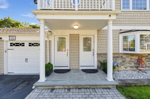 A two-story house with a covered front porch, two garage doors, and a welcome sign with sunflowers.