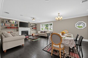 Un salon spacieux avec une cheminée, un coin repas avec une table et des chaises, et une bibliothèque remplie de livres.