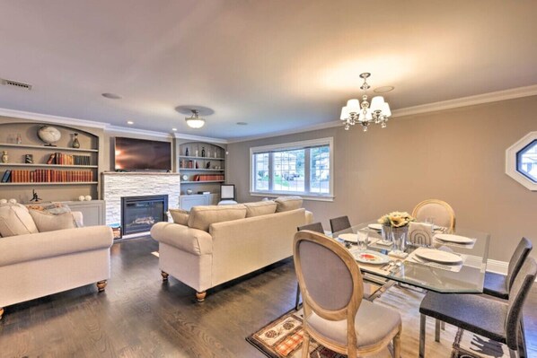 A spacious living room with a fireplace, a dining area with a glass table, and a cozy seating area with a sofa and chairs.