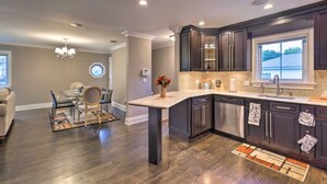A modern kitchen with dark cabinetry, a large island, and a dining area with a chandelier.