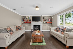 Ein Wohnzimmer mit zwei Sofas, einem Couchtisch, einem Kamin, Bücherregalen und einem Fernseher.