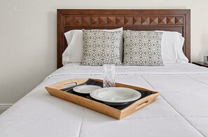 A neatly made bed with a wooden headboard, two patterned pillows, and a tray with plates and a glass of water. - Cozy Glen Cove Apt Near Ferry, Parking & NYC! (Glen Cove)