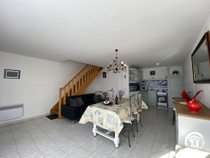 Un salon comprenant une table à manger, des chaises, un canapé, un escalier, un coin cuisine et un vase rouge posé sur un comptoir.