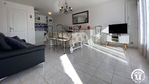 Un salon comprenant un canapé, une table à manger, des chaises, un lustre et un téléviseur.