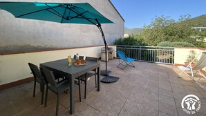 Une terrasse avec une table, des chaises, un parasol de couleur turquoise et une vue sur le paysage environnant.