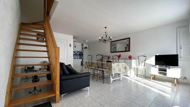 Un salon avec un escalier, un coin repas, une cuisine et un téléviseur posé sur un meuble.