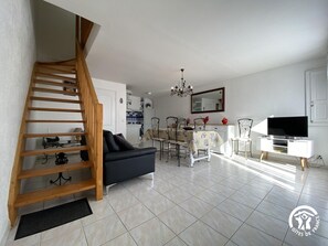 A living room with a staircase, a dining area, a kitchen, and a TV on a stand.