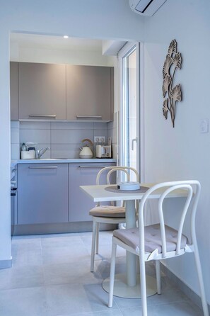 A modern kitchen with grey cabinets, a white countertop, and a dining area with a white table and chairs. - L'Harmonie de Carnot avec Balcon (Cannes)