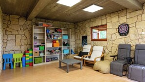 Una habitació amb pared de pedra, un joc de fletxes, una prestatgeria i dues cadires.
