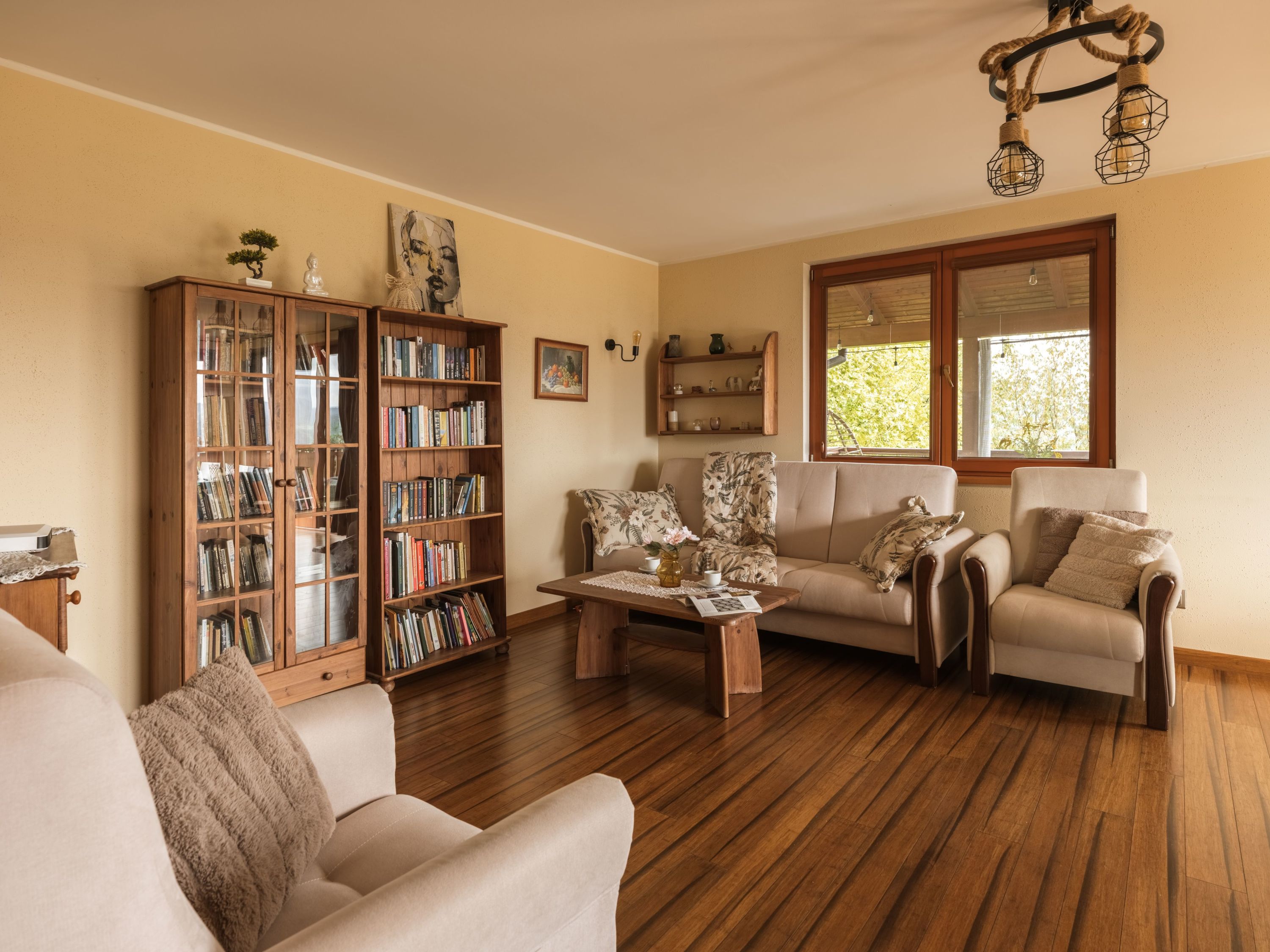 Una sala de estar con piso de madera, un sofá, una mesa de centro, una estantería y un ventanal con vistas.