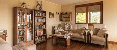 Una sala de estar con piso de madera, un sofá, una mesa de centro, una estantería y un ventanal con vistas.