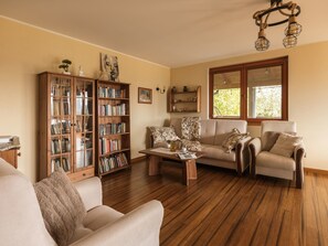 A living room with a wooden floor, a sofa, a coffee table, a bookshelf, and a window with a view.