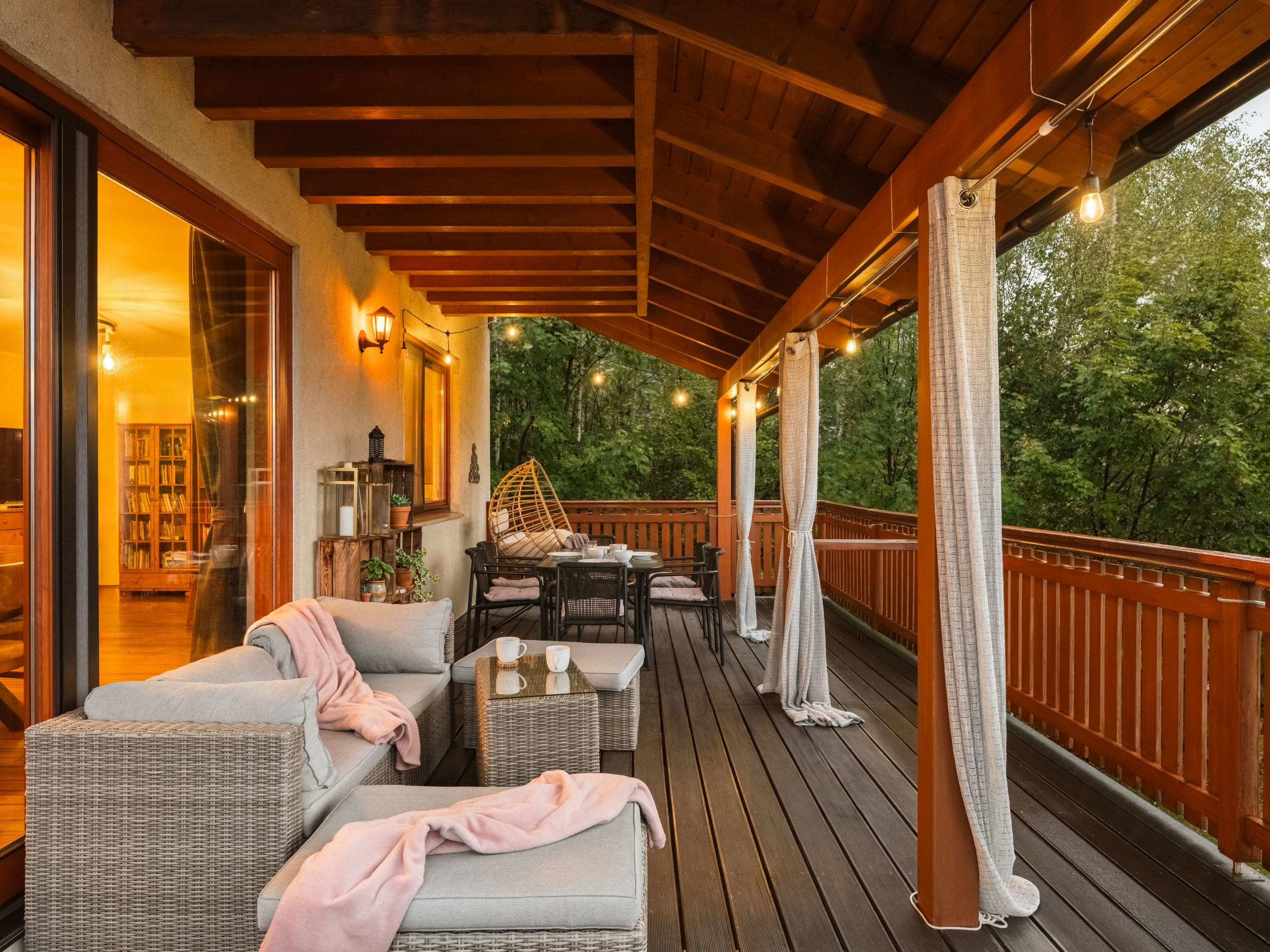 Un espace extérieur aménagé avec des meubles en osier, une table avec des tasses et une vue sur les arbres.