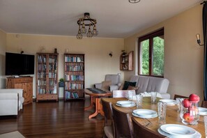 A living room with a wooden dining table set for four, a sofa, a television, and two bookshelves filled with books. - House with a View, Mucharz 405 (Mucharz)