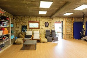 A room with a stone wall, a dartboard, a treadmill, and exercise chairs.