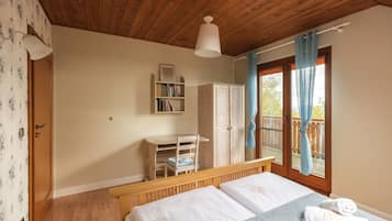 A bedroom with a wooden ceiling, a bed with white linens, a wooden desk, a wardrobe, and a window with curtains.