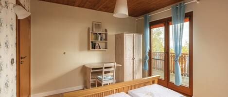 Une chambre avec un plafond en bois, un lit recouvert de draps blancs, un bureau en bois, une armoire et une fenêtre avec des rideaux.