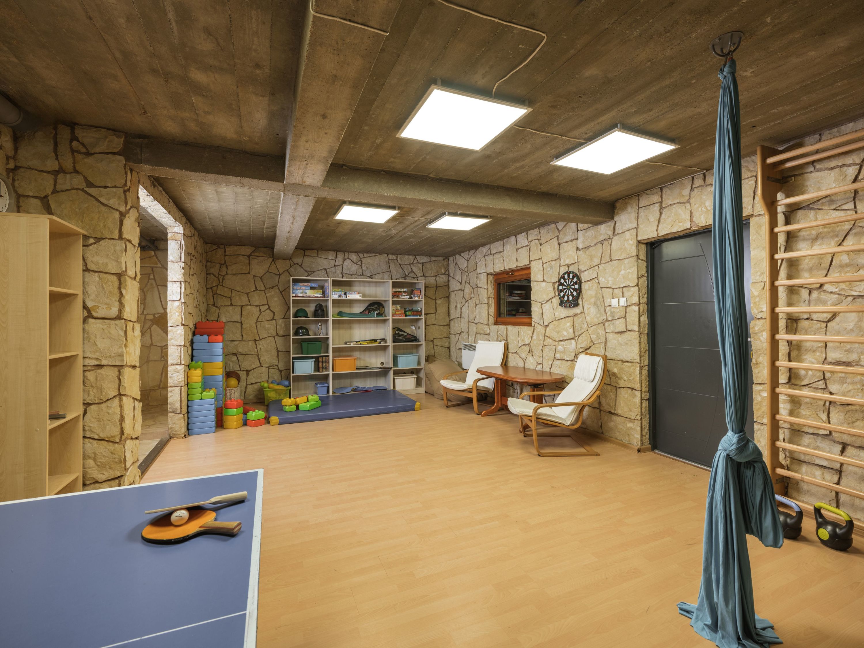 A room with a ping pong table, shelves with toys, a dartboard, and a yoga mat.