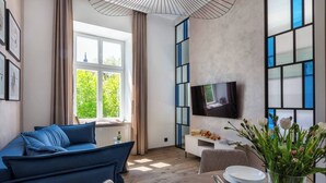 Una sala de estar moderna con un sofá azul, un televisor de pantalla plana, una mesa de comedor con platos y una ventana con cortinas.