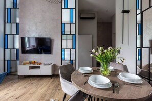 A modern dining area with a round table, chairs, a vase of flowers, and a flat-screen TV mounted on the wall. - Canvas House Apartament Oasis (Kraków)