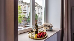 Una ventana con vistas a edificios, una botella de vino, una bandeja con fresas y una pila de libros en el alféizar.