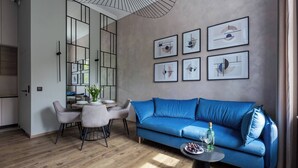 Una sala de estar moderna con un sofá azul, una mesa de comedor con sillas, y una cocina visible a través de un separador de vidrio.