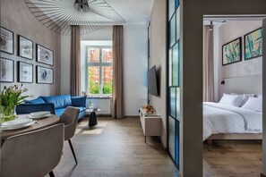 A modern hotel room with a blue sofa, a dining table with plates, a coffee table, a bed, and artwork on the walls. - Canvas House Apartament Oasis (Kraków)
