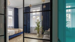 Ein Schlafzimmer mit einem Bett, einer Zimmerpflanze, einem Sessel und einem großen Fenster mit Vorhängen.
