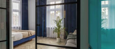 A bedroom with a bed, a potted plant, a chair, and a large window with curtains.