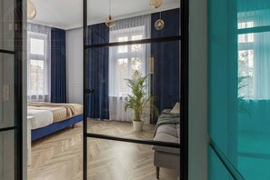 Ein Schlafzimmer mit einem Bett, einer Zimmerpflanze, einem Sessel und einem großen Fenster mit Vorhängen.