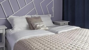 Ein ordentlich bezogenes Bett mit einer gesteppten Decke, zwei Nachttische mit Schubladen und ein Kopfteil mit geometrischem Muster.