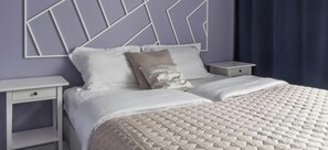 Ein ordentlich bezogenes Bett mit einer gesteppten Decke, zwei Nachttische mit Schubladen und ein Kopfteil mit geometrischem Muster.