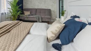 Ein Schlafzimmer mit einem Bett, einem grauen Sofa, einer Topfpflanze und einem Fenster mit Vorhängen.