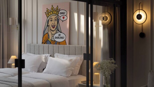 Ein modernes Schlafzimmer mit einem großen Bett, Nachttischlampen, einer Wanddekoration und einer Vase mit Blumen.