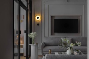A modern living room with a grey sofa, a round table with a vase of flowers, a wall-mounted TV, and a tall floor lamp. - Sandstone 2-Bed Apartment in the Heart of Kraków (Kraków)