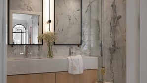 Ein modernes Badezimmer mit Marmorwaschtisch, einem großen Spiegel, einer Duschkabine und einer Vase mit Blumen.