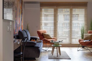 A modern living room with a sofa, armchairs, a coffee table, and a large window with blinds. - Cozy & Family-Friendly 2-bed Apartment (Kraków)