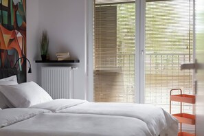 A bedroom with a bed, a radiator, a shelf with books and a plant, and a window with blinds. - Cozy & Family-Friendly 2-bed Apartment (Kraków)