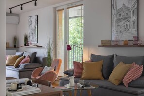 A modern living room with a grey sofa, a brown armchair, and a coffee table with a book and a cup. - Modern 2-Bed Apartment with 2 Bathrooms, Balcony (Kraków)