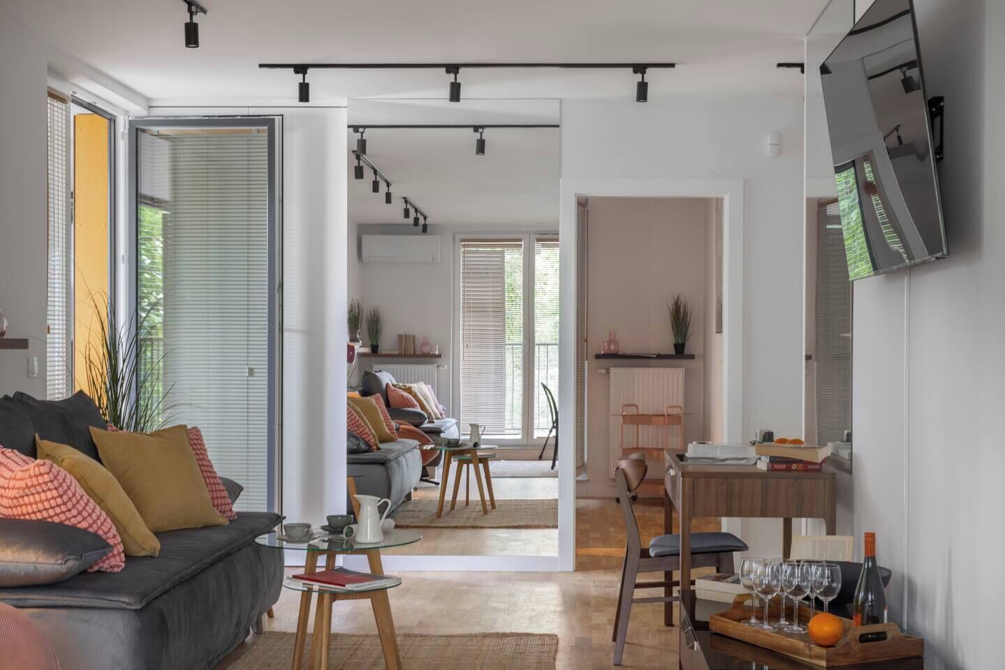 Un espacio habitable moderno con sofá, mesa de comedor y sillas, una zona de cocina y un televisor en la pared.