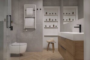 A modern bathroom with a toilet, a glass shower enclosure, a white sink with a black faucet, and shelves with potted plants. - Modern 2-Bed Apartment with 2 Bathrooms, Balcony (Kraków)